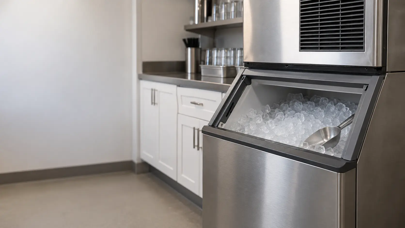 A restaurant back room with a modular ice machine on its bin and white shaker cabinets, seen close at the ice machine's bin door.