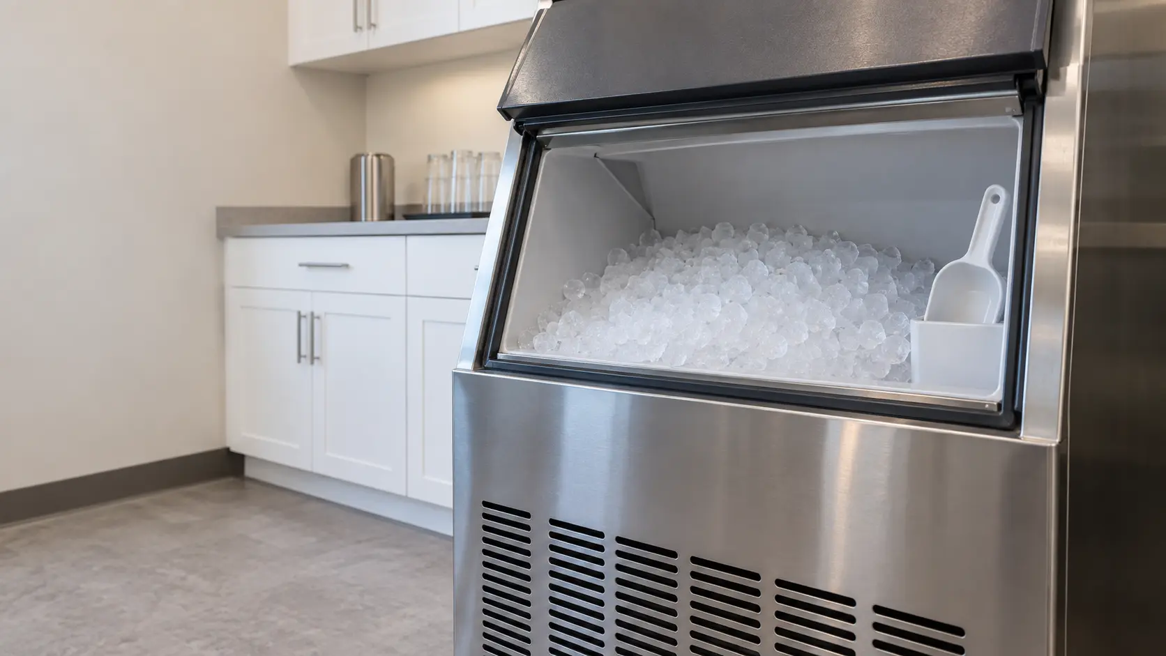 An office break room with a nugget ice machine and white shaker cabinets, seen close at the ice machine's bin door.