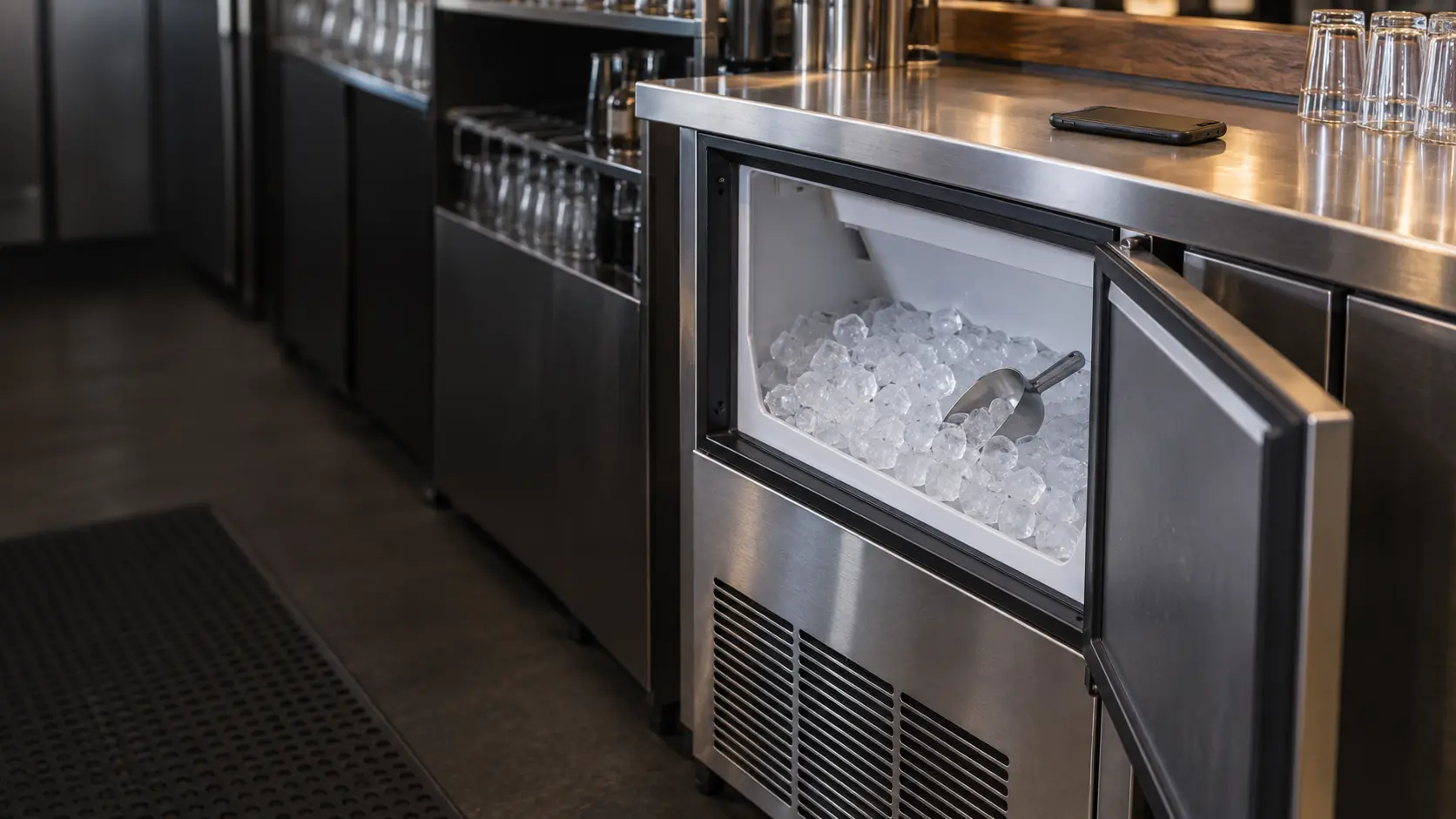 A bar counter with a phone lying face down above an undercounter ice machine.
